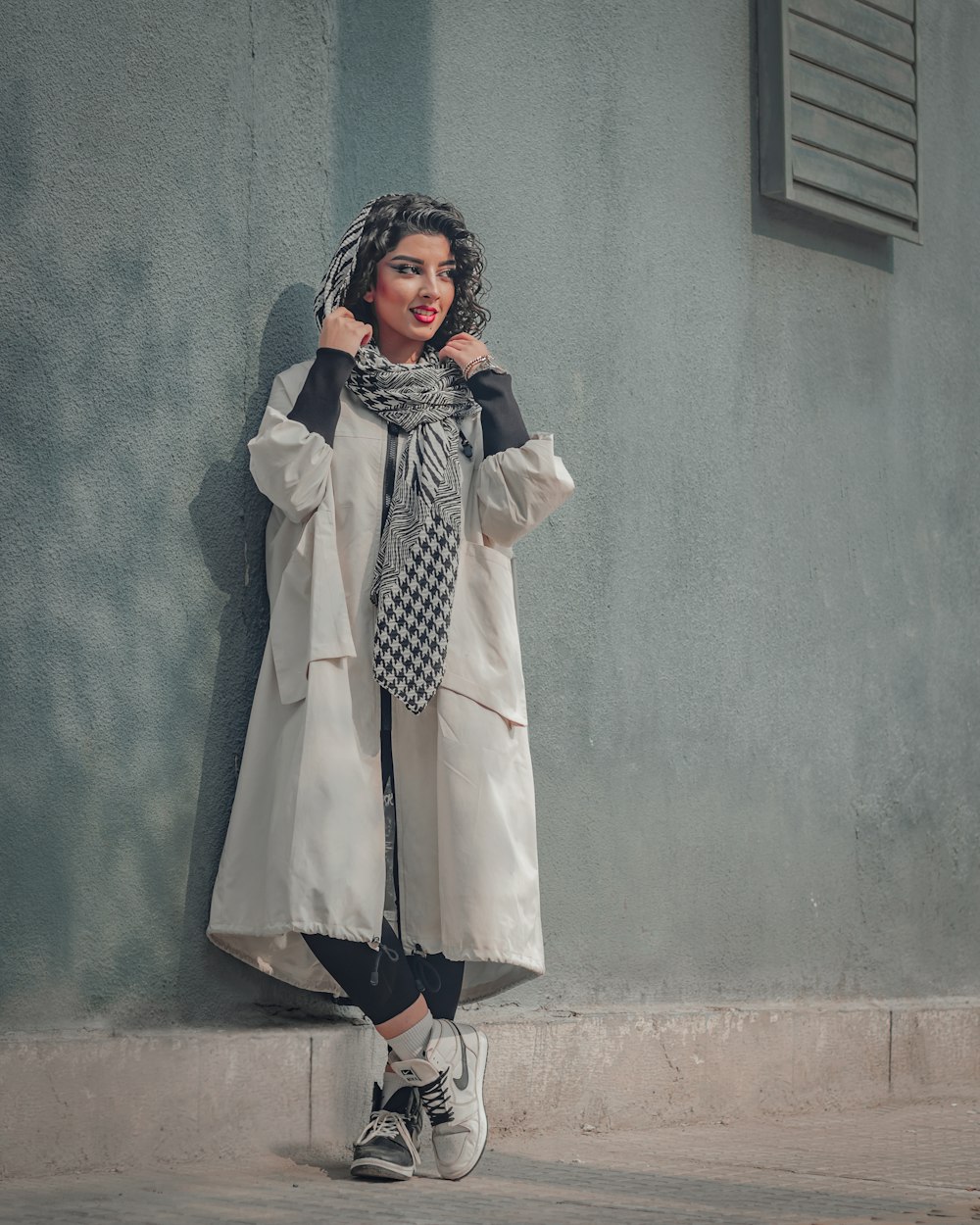 Woman wearing a light coat and patterned scarf on a city sidewalk